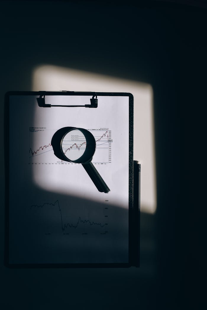 services-03 A magnifying glass lays over a financial chart on a clipboard, casting intriguing shadows.